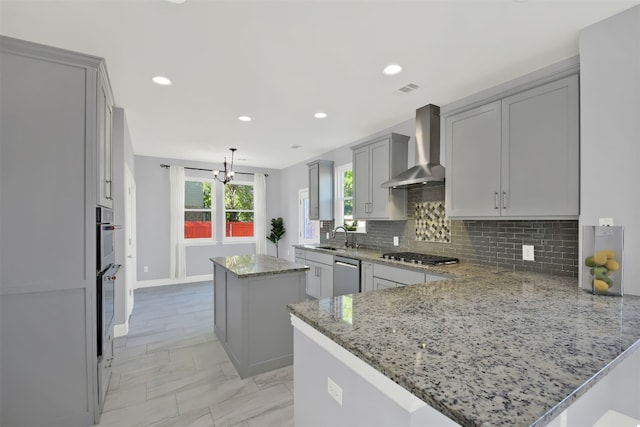 kitchen featuring a center island, stainless steel appliances, wall chimney range hood, light stone counters, and kitchen peninsula