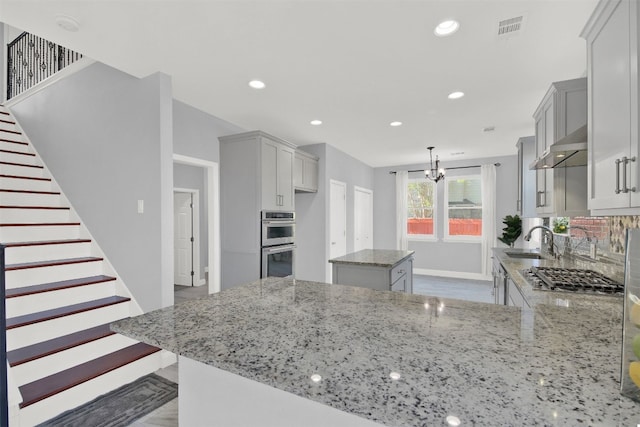 kitchen featuring kitchen peninsula, stainless steel appliances, light stone counters, and sink