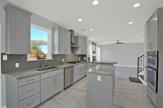 kitchen with wall chimney range hood, stainless steel appliances, gray cabinets, and sink