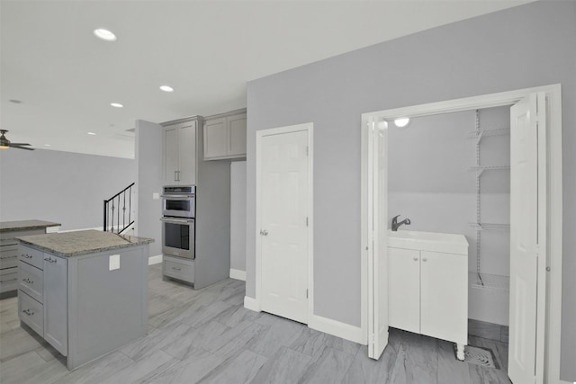 kitchen featuring double oven, gray cabinetry, ceiling fan, and a kitchen island