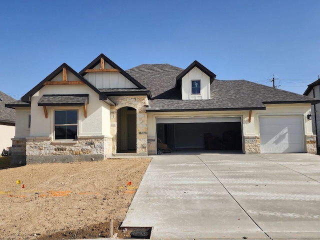 view of front of home with a garage, stone siding, a shingled roof, and concrete driveway