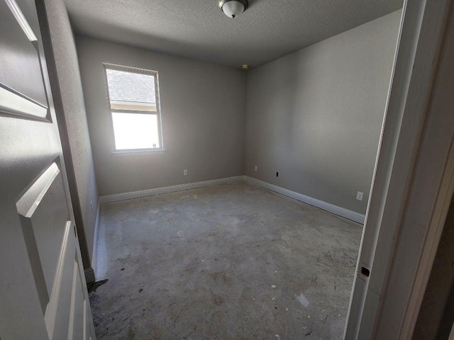 empty room with unfinished concrete floors, baseboards, and a textured ceiling