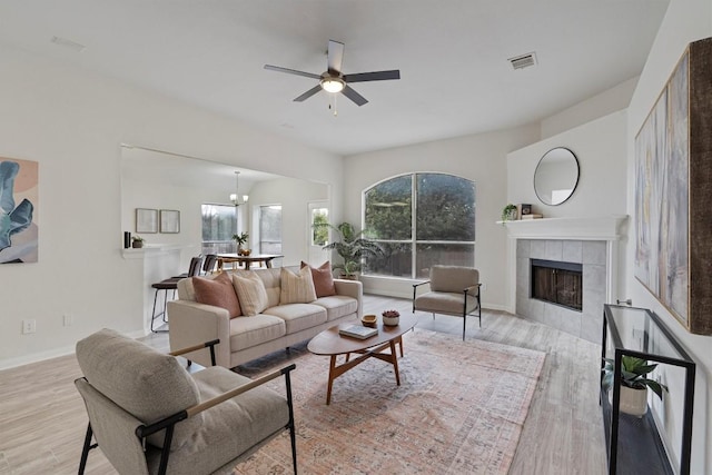 living room featuring ceiling fan with notable chandelier, light wood-type flooring, and a tiled fireplace