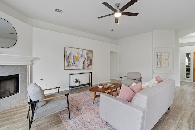 living room with a tile fireplace, light hardwood / wood-style flooring, and ceiling fan