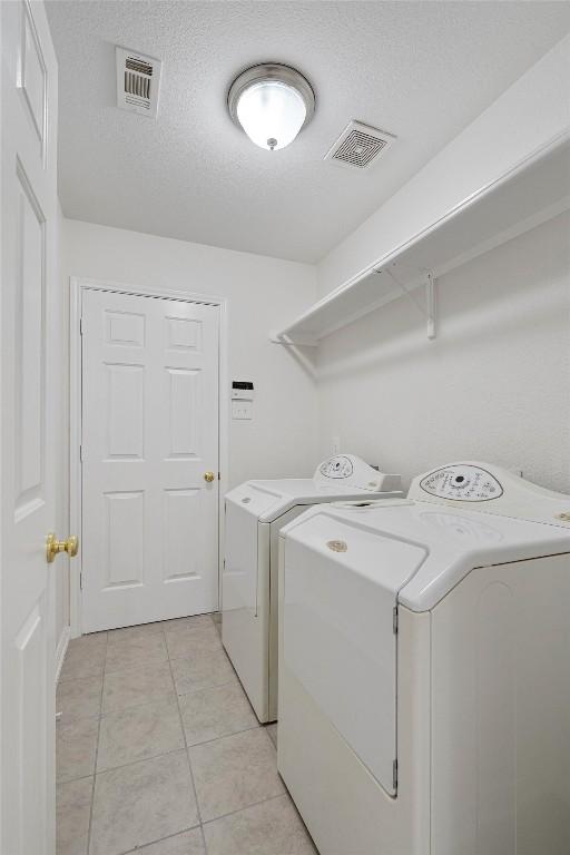 clothes washing area featuring light tile patterned floors, a textured ceiling, and washing machine and clothes dryer