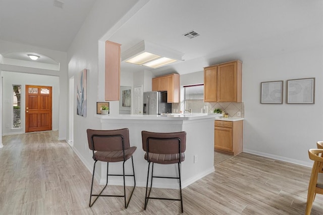 kitchen featuring light wood-type flooring, stainless steel refrigerator with ice dispenser, backsplash, and plenty of natural light