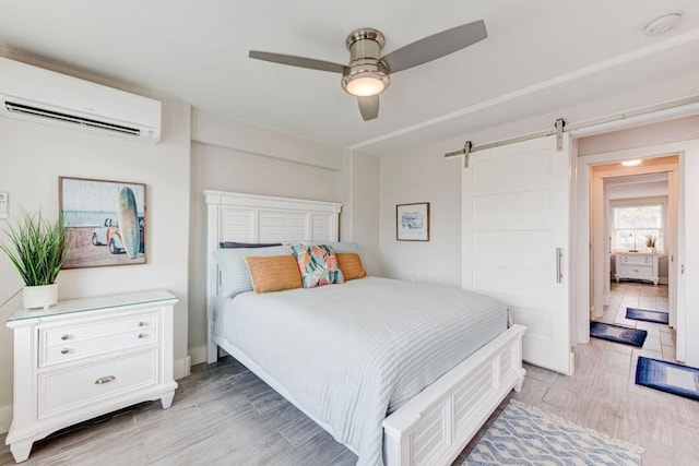 bedroom with a barn door, ceiling fan, and a wall mounted air conditioner