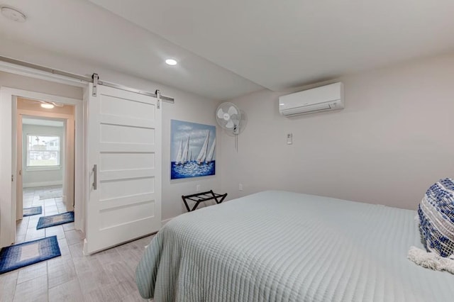 bedroom featuring an AC wall unit, a barn door, and light hardwood / wood-style floors