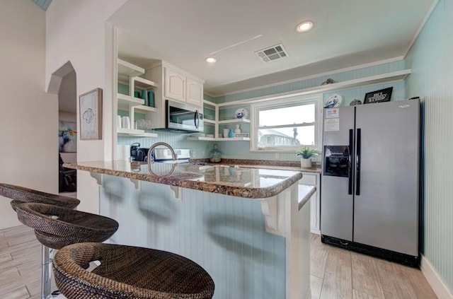 kitchen with kitchen peninsula, appliances with stainless steel finishes, a kitchen breakfast bar, dark stone counters, and white cabinetry