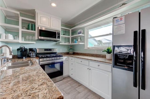 kitchen with light stone countertops, appliances with stainless steel finishes, white cabinetry, and sink