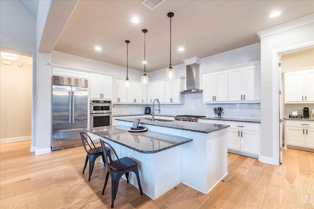 kitchen with stainless steel appliances, visible vents, a sink, wall chimney range hood, and a kitchen bar