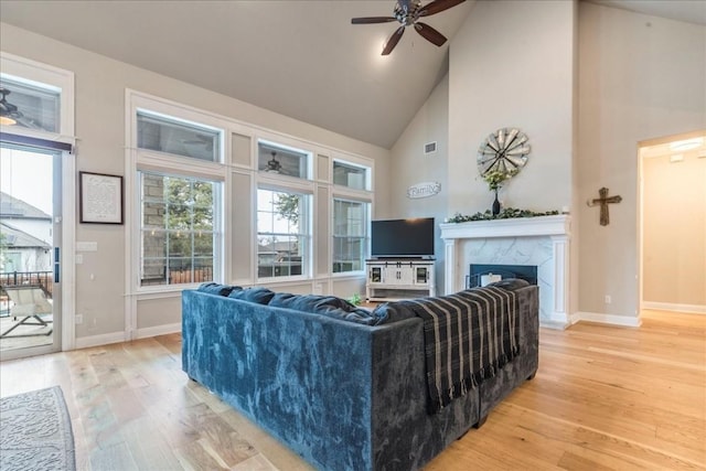 living room with light wood finished floors, baseboards, visible vents, a fireplace, and high vaulted ceiling