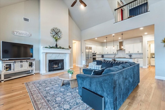 living room with a high end fireplace, high vaulted ceiling, light hardwood / wood-style floors, and ceiling fan