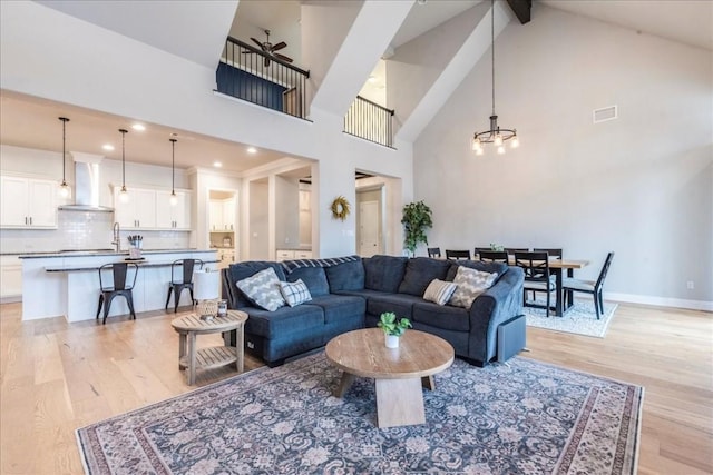 living area with baseboards, visible vents, beamed ceiling, light wood-type flooring, and high vaulted ceiling