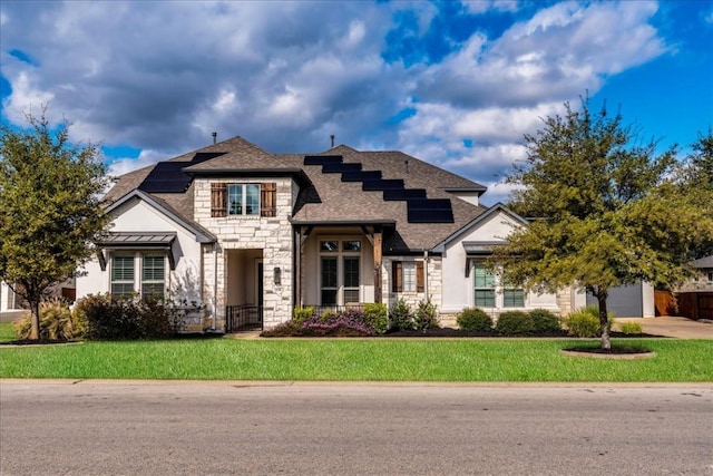 view of front facade featuring a shingled roof, concrete driveway, stone siding, roof mounted solar panels, and a front lawn