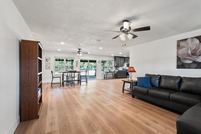 living room with ceiling fan, light hardwood / wood-style floors, and a textured ceiling