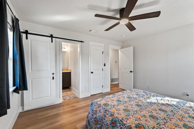 bedroom featuring a barn door, ceiling fan, ensuite bath, and light wood-type flooring