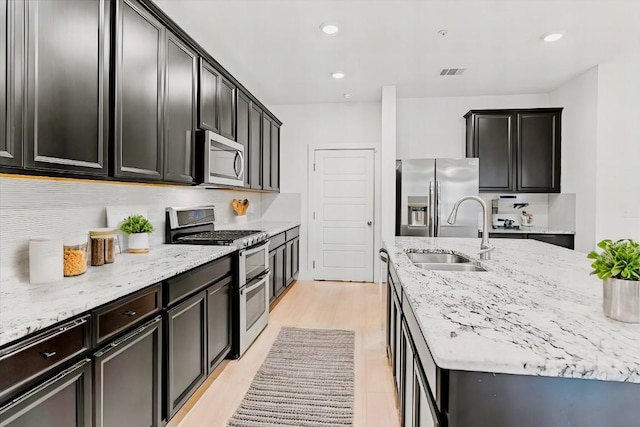 kitchen with sink, stainless steel appliances, tasteful backsplash, light stone counters, and light wood-type flooring