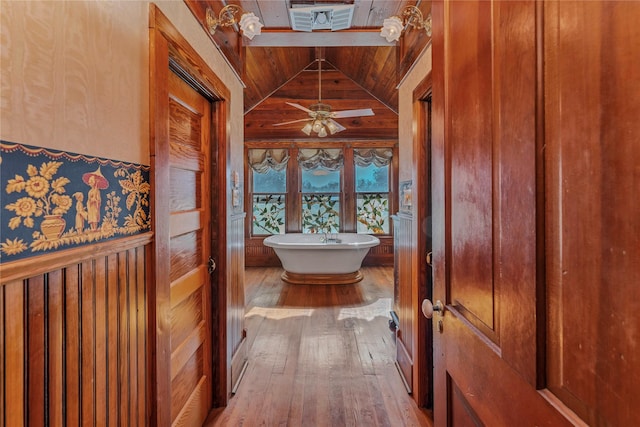 bathroom featuring a bath, wood-type flooring, wood walls, and vaulted ceiling