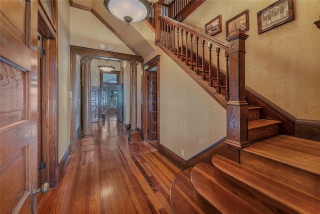 stairs with hardwood / wood-style floors, a towering ceiling, and decorative columns