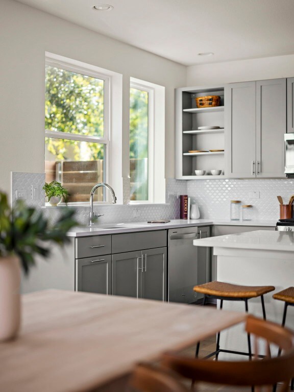 kitchen with dishwasher, a kitchen bar, gray cabinets, and tasteful backsplash