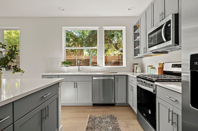 kitchen with decorative backsplash, appliances with stainless steel finishes, sink, light hardwood / wood-style flooring, and gray cabinets