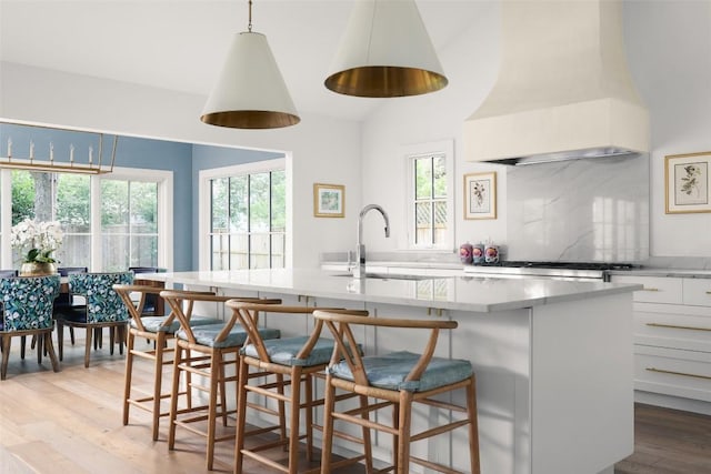 kitchen featuring a kitchen island with sink, white cabinets, a kitchen breakfast bar, sink, and decorative light fixtures