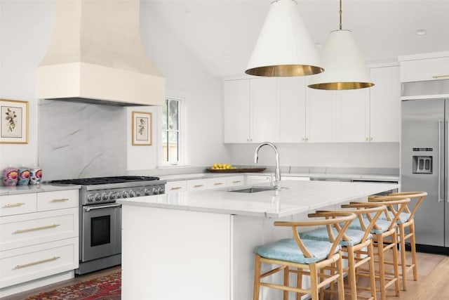 kitchen with high end appliances, sink, a center island with sink, white cabinets, and custom exhaust hood