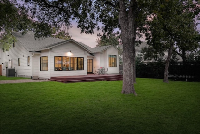 back house at dusk featuring a lawn, a wooden deck, and central AC