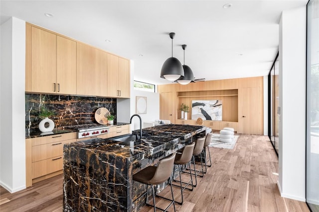 kitchen with a breakfast bar area, light brown cabinets, a sink, decorative backsplash, and modern cabinets