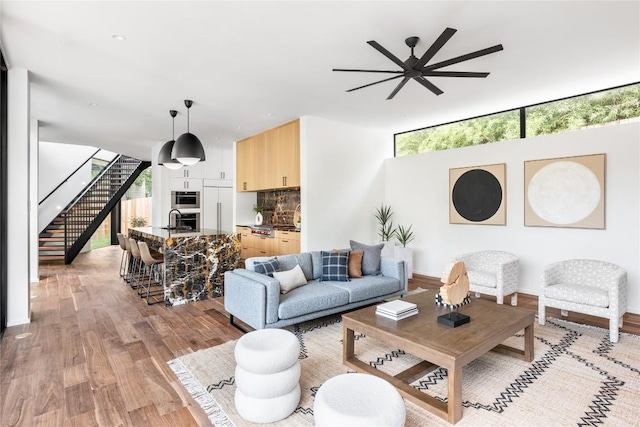 living area with ceiling fan, light wood-style flooring, and stairs