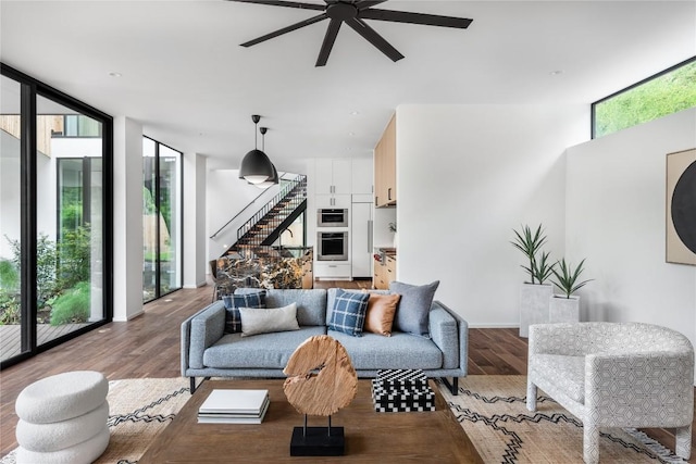 living room featuring baseboards, ceiling fan, stairway, wood finished floors, and a wall of windows