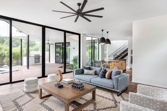 living room with stairway, expansive windows, ceiling fan, and light wood-style flooring