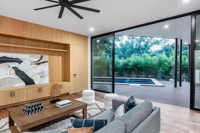 living area featuring a ceiling fan, expansive windows, wooden walls, and wood finished floors