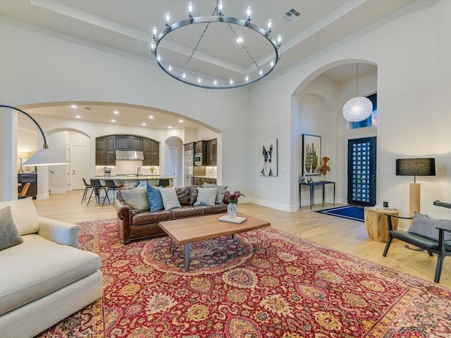 living room with a notable chandelier, light hardwood / wood-style floors, a towering ceiling, and sink