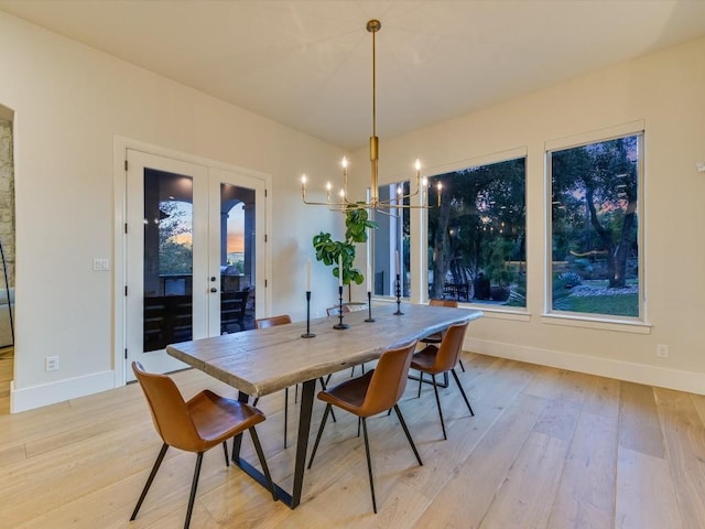 dining room with a notable chandelier, light wood-type flooring, and french doors