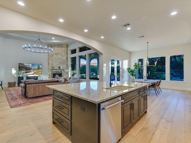 kitchen featuring a fireplace, an island with sink, hanging light fixtures, and sink