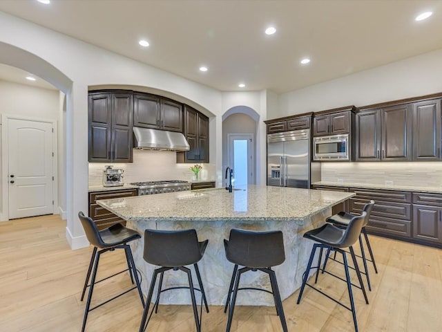 kitchen featuring a breakfast bar area, built in appliances, and a kitchen island with sink