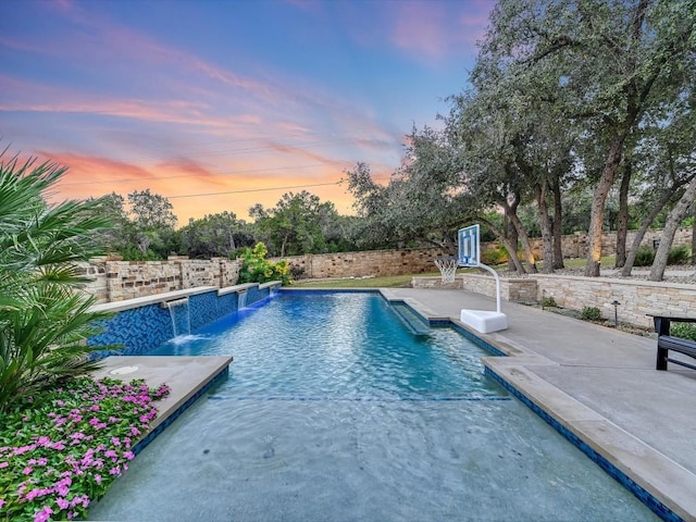 pool at dusk with pool water feature and a patio