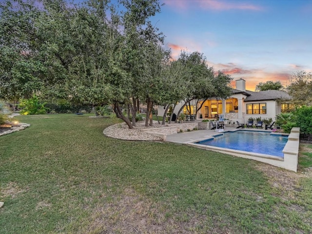 pool at dusk with a lawn and a patio area