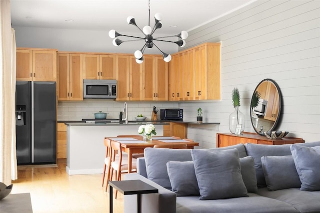 kitchen featuring fridge with ice dispenser, stainless steel microwave, backsplash, dark countertops, and open floor plan