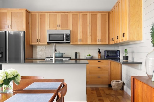 kitchen featuring tasteful backsplash, light brown cabinets, stainless steel appliances, and dark countertops