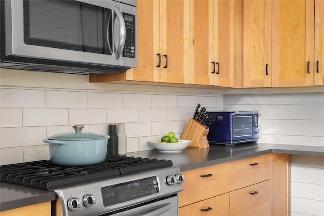 kitchen with dark countertops, decorative backsplash, appliances with stainless steel finishes, and light brown cabinetry