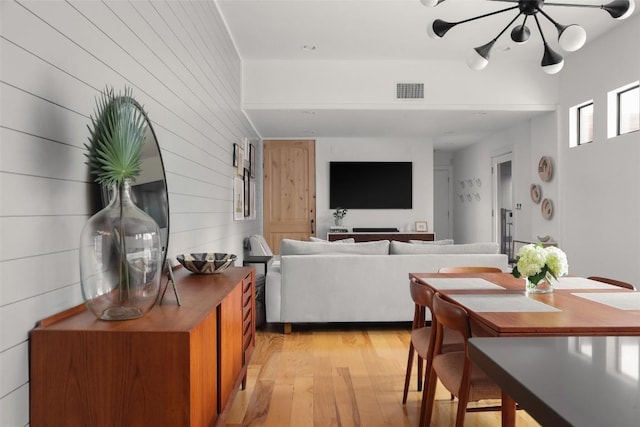 dining room with visible vents, wooden walls, a ceiling fan, and light wood finished floors