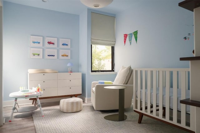 bedroom featuring baseboards, a nursery area, and wood finished floors