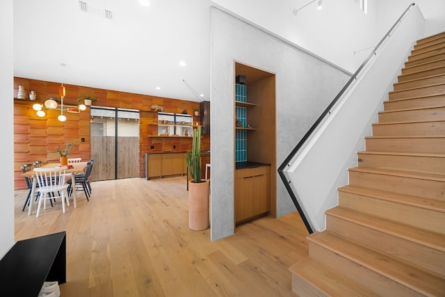 stairs featuring hardwood / wood-style floors, wooden walls, and a chandelier