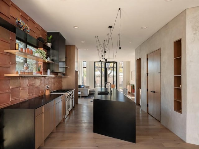 kitchen featuring sink, hanging light fixtures, a center island with sink, stainless steel stove, and light wood-type flooring