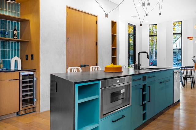 kitchen with a center island with sink, sink, wine cooler, light wood-type flooring, and stainless steel appliances