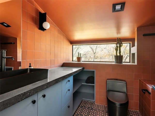 bathroom with tile patterned flooring, vanity, vaulted ceiling, and tile walls