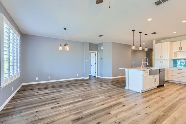 kitchen featuring pendant lighting, dishwasher, white cabinets, a center island with sink, and light hardwood / wood-style floors